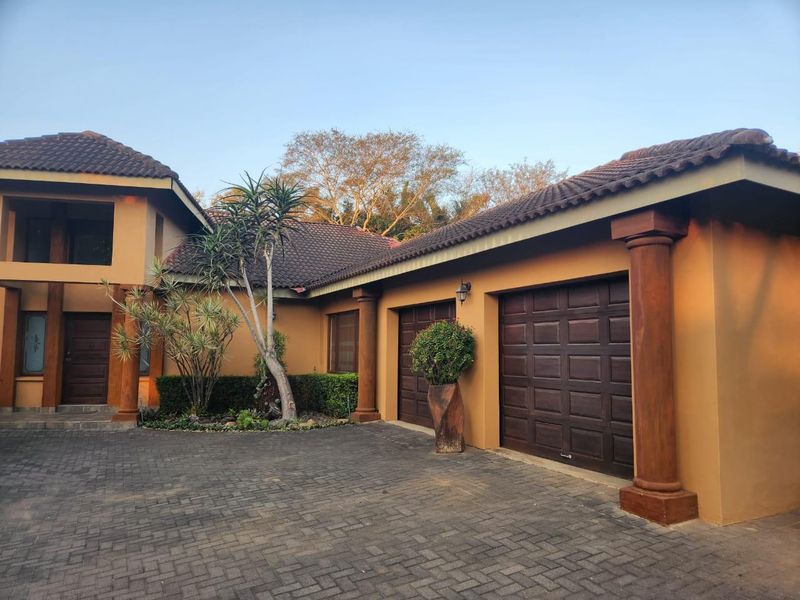 Front elevation of a residential property featuring a paved driveway, double garage with paneled doors, and decorative architectural columns.