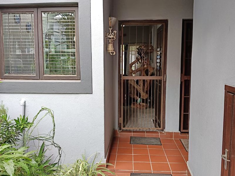 A private apartment entrance featuring a security gate, tiled porch area, and a window with fitted blinds.