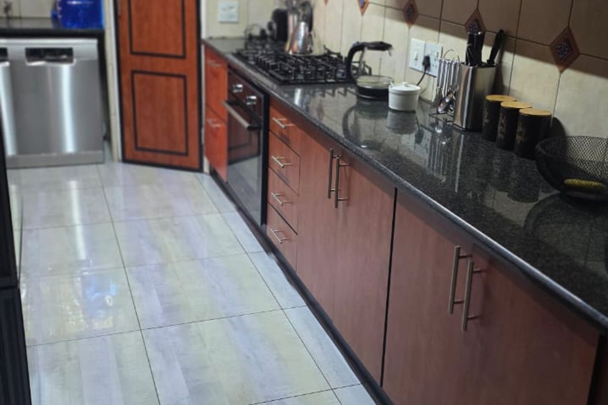 A functional galley-style kitchen featuring wood-finish cabinetry, granite countertops, a built-in gas hob, oven, and tiled flooring.