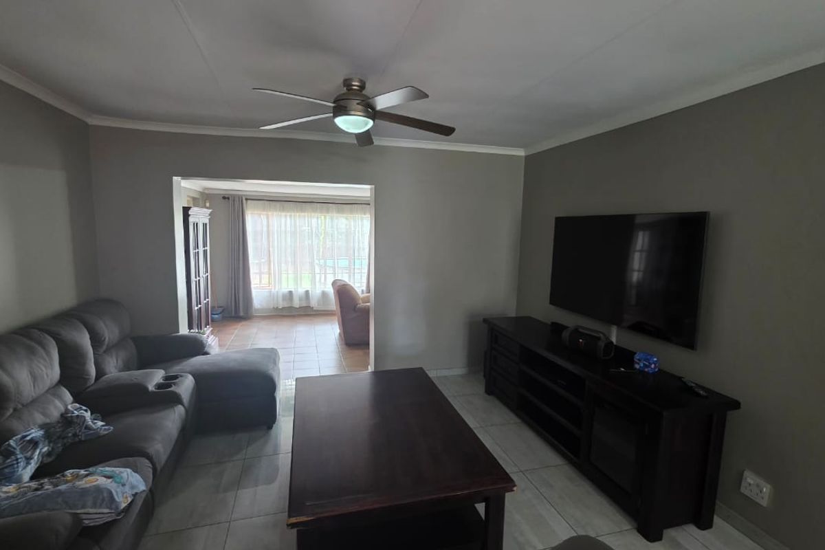 A comfortable living room featuring neutral wall tones, tiled flooring, and a ceiling fan, with an open transition to an adjacent sunlit space.
