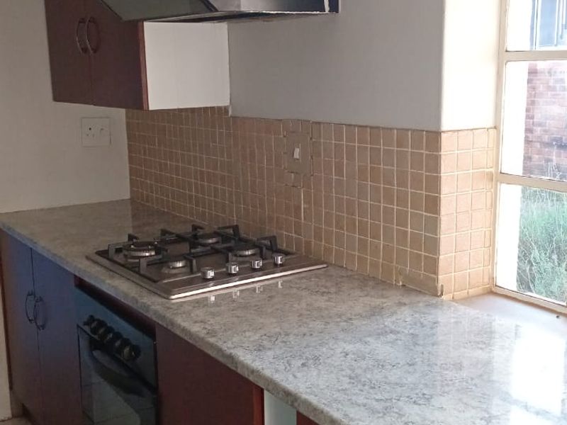 A functional kitchen area featuring a gas hob, built-in oven, extractor fan, and laminate countertops, requiring minor repairs to cabinetry and finishes.
