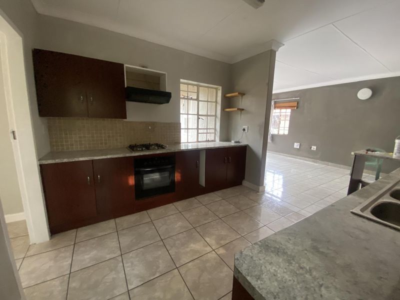 Open-plan kitchen featuring dark wood cabinetry, gas hob, built-in oven, and tiled flooring, flowing into an adjacent living area.