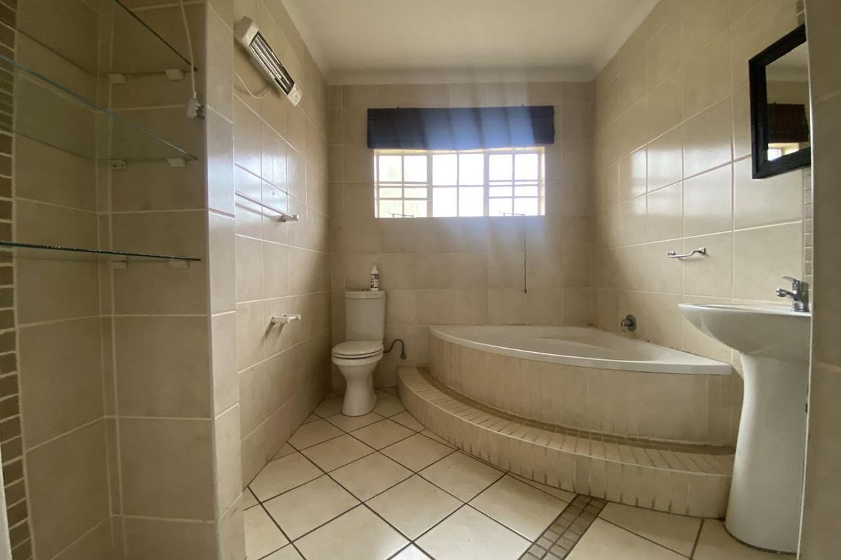 A functional bathroom featuring a built-in corner bathtub, pedestal basin, and neutral ceramic tiling throughout.