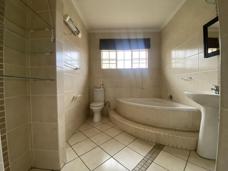 A functional bathroom featuring a built-in corner bathtub, pedestal basin, and neutral ceramic tiling throughout.
