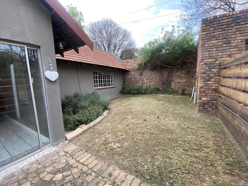A private rear garden featuring a paved patio area, brick boundary walls, and a sliding door entrance to the cottage interior.