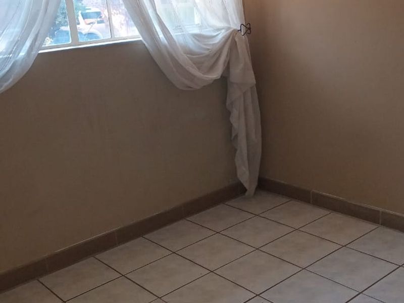 A vacant bedroom featuring neutral wall tones, ceramic floor tiling, and a window fitted with security bars.