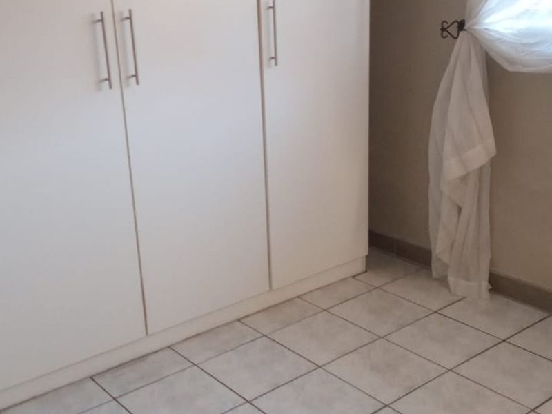 A clean, empty bedroom featuring neutral tiled flooring and a functional built-in wardrobe with modern handles.