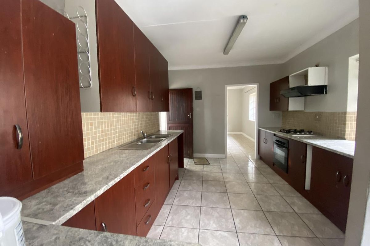 A functional galley-style kitchen featuring dark wood cabinetry, laminate countertops, a built-in oven with gas hob, and neutral tiled flooring.
