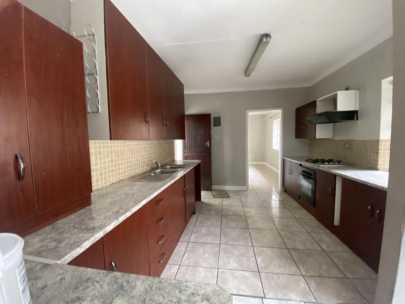 A functional galley-style kitchen featuring dark wood cabinetry, laminate countertops, a built-in oven with gas hob, and neutral tiled flooring.