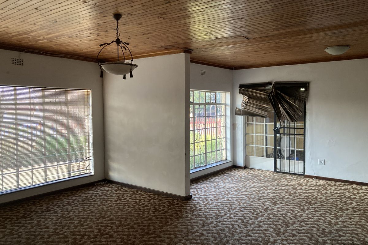 Spacious living area featuring a timber tongue and groove ceiling, large windows with security bars, and direct access to the exterior via a security gate.