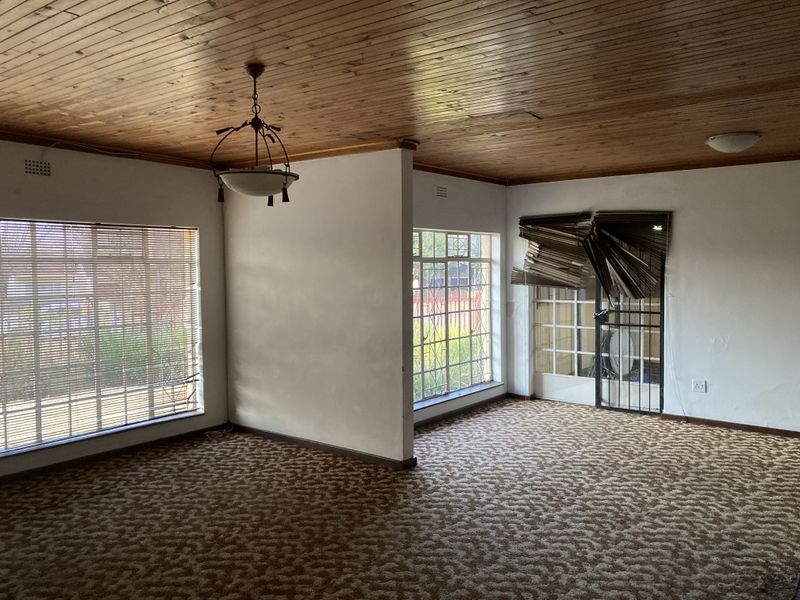 Spacious living area featuring a timber tongue and groove ceiling, large windows with security bars, and direct access to the exterior via a security gate.