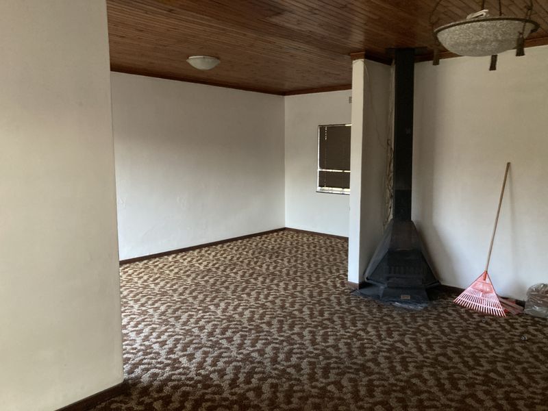 An empty living room featuring a timber-clad ceiling, patterned carpeting, and a prominent freestanding fireplace, offering a blank canvas for renovation.