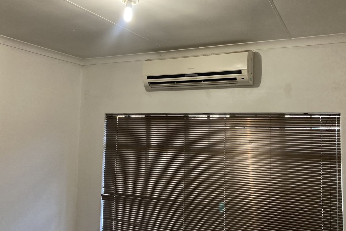 A bedroom featuring a wall-mounted split-system air conditioner and fitted venetian blinds, requiring minor cosmetic updates to the wall finishes.