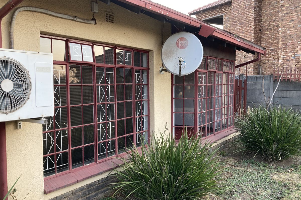 Rear exterior view of the property featuring metal-framed windows with security bars, an external air conditioning unit, and a satellite dish.