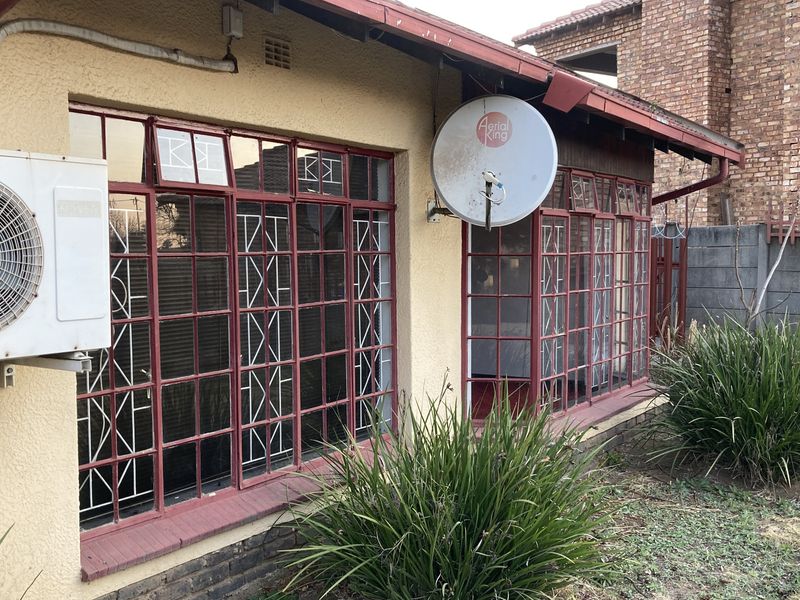 Rear exterior view of the property featuring metal-framed windows with security bars, an external air conditioning unit, and a satellite dish.