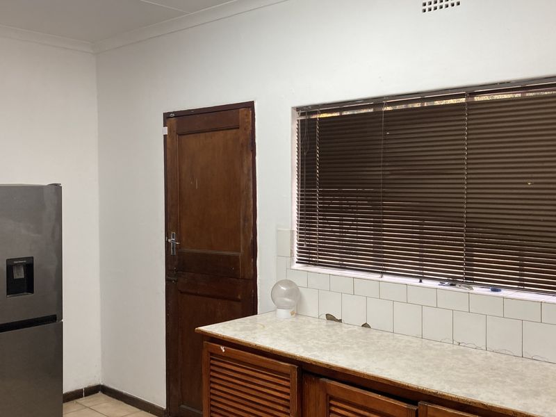 A functional kitchen area featuring timber cabinetry, a tiled backsplash, and a laminate countertop, requiring cosmetic updates to modernize the space.