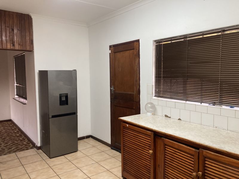 Kitchen area featuring wooden cabinetry, tiled flooring, and a tiled backsplash, requiring cosmetic updates to modernize the space.