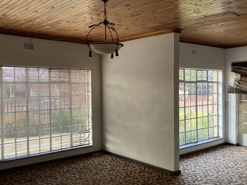 Spacious living area featuring a timber tongue and groove ceiling, large steel frame windows with security bars, and neutral wall finishes.