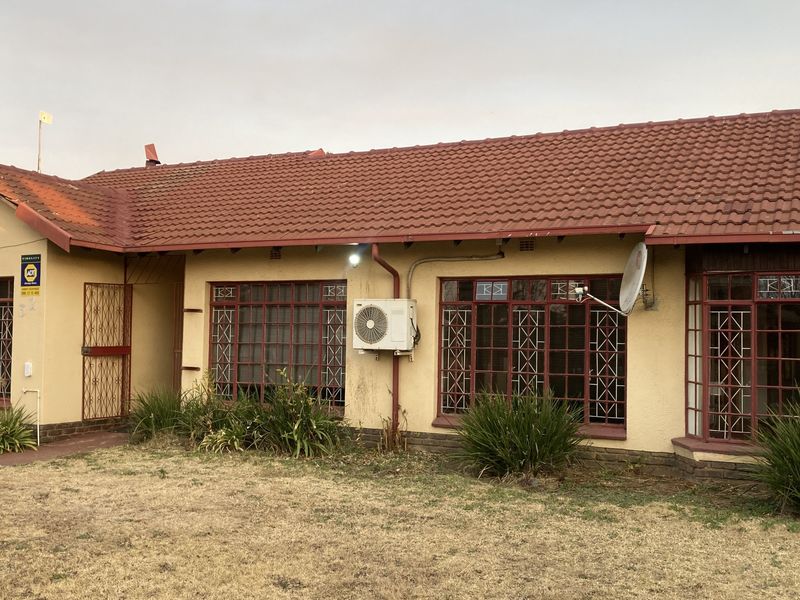 Front elevation of a single-story house featuring a tiled roof, security bars on windows, and an exterior air conditioning unit.