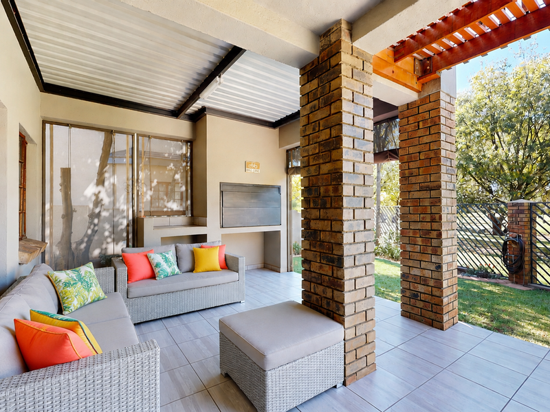 Covered patio featuring a built-in braai, brick support pillars, and tiled flooring, overlooking a private garden area.
