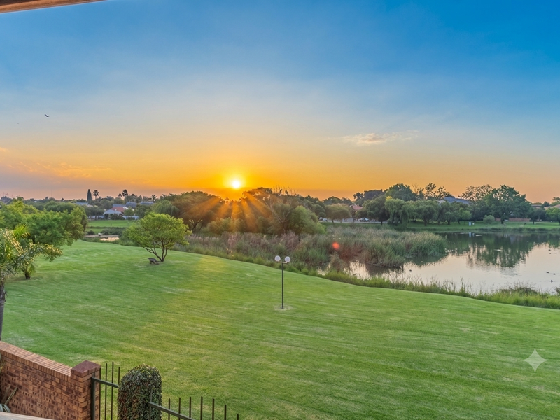 Scenic sunset view overlooking a lush green lawn, natural pond, and surrounding landscape, captured from an elevated vantage point.