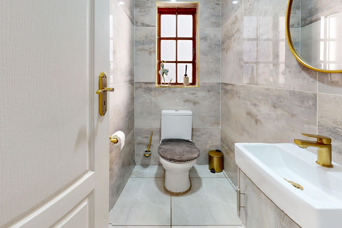 A modern guest bathroom featuring neutral wall and floor tiles, a vanity basin with brass fixtures, and a window for natural light.