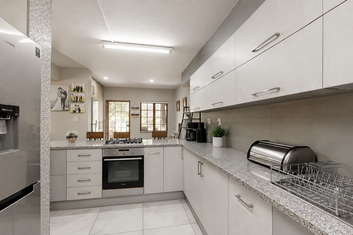 Modern kitchen featuring light-toned cabinetry, granite countertops, a gas hob, built-in oven, and tiled flooring, offering a clean and functional workspace.