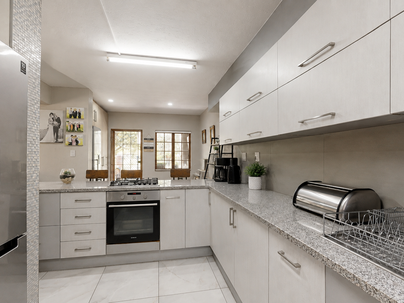 Modern kitchen featuring light-toned cabinetry, granite countertops, a gas hob, built-in oven, and tiled flooring, offering a clean and functional workspace.