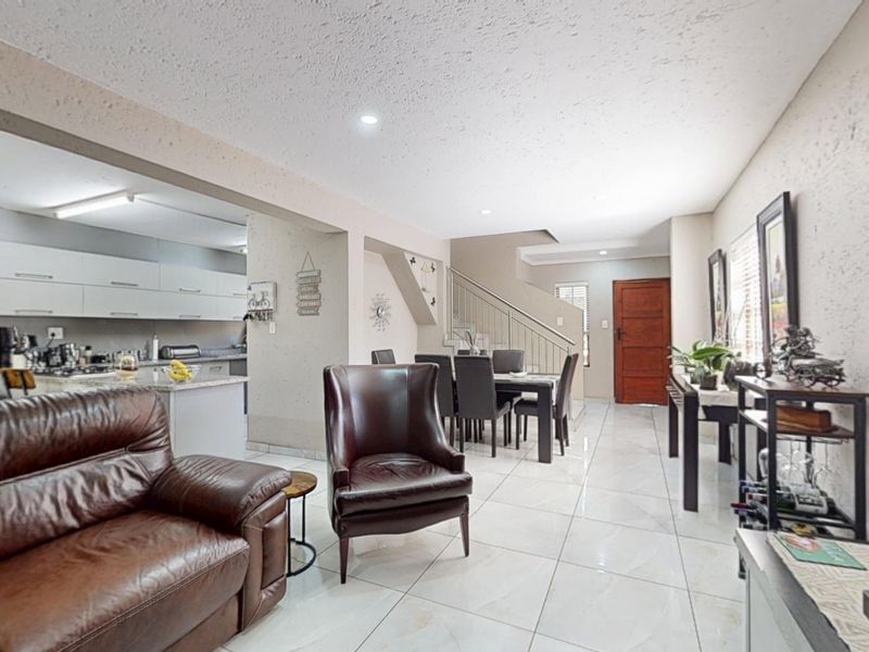 Open-plan living and dining area featuring tiled flooring, a modern kitchen with stone countertops, and a staircase leading to the upper level.