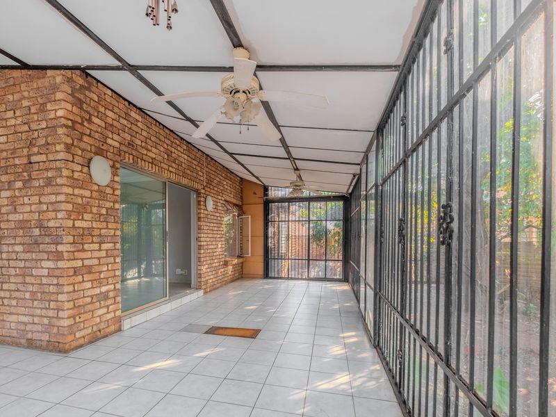 Enclosed patio area featuring exposed brick walls, tiled flooring, ceiling fans, and secure metal screening, providing a versatile outdoor living space.