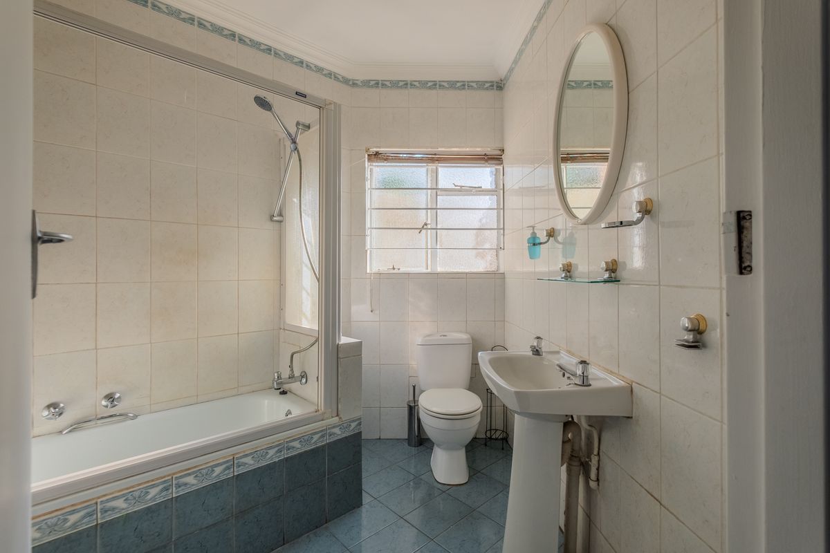 A functional bathroom featuring a pedestal basin, toilet, and a combined bathtub and shower unit with tiled finishes.