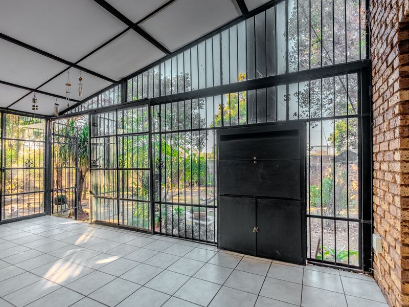 Enclosed patio area featuring tiled flooring, an exposed brick wall, and a built-in braai, offering a versatile space with views of the garden.