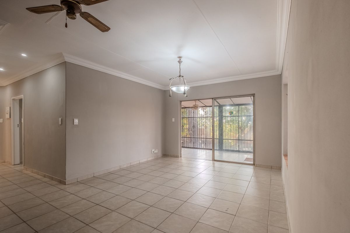 Spacious, empty living area featuring neutral tiled flooring, ceiling fan, and sliding glass doors providing access to an enclosed patio.