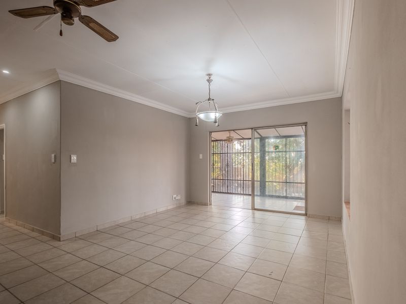 Spacious, empty living area featuring neutral tiled flooring, ceiling fan, and sliding glass doors providing access to an enclosed patio.
