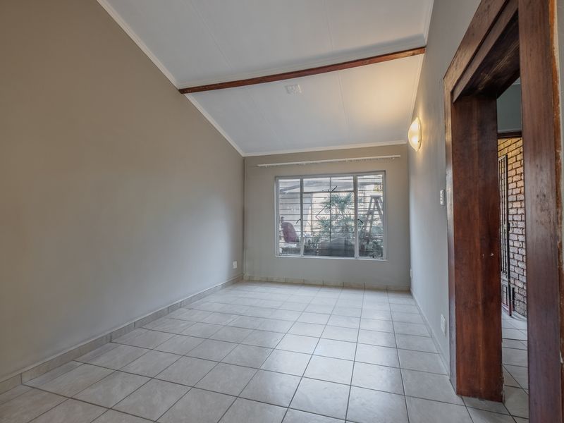 A bright, empty living area featuring tiled flooring, a vaulted ceiling with an exposed timber beam, and a large window providing natural light.