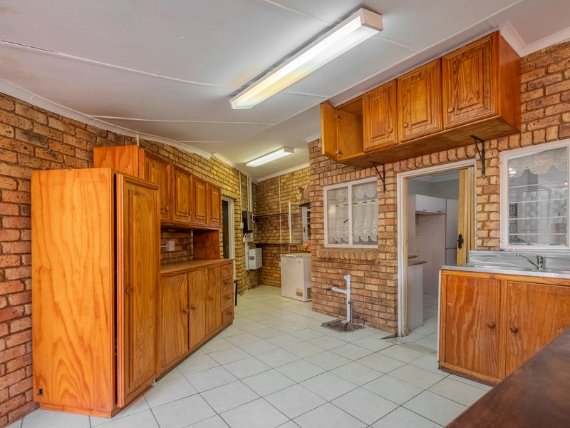 A rustic kitchen featuring exposed brick walls, wooden cabinetry, and tiled flooring, offering a functional space with potential for modern updates.