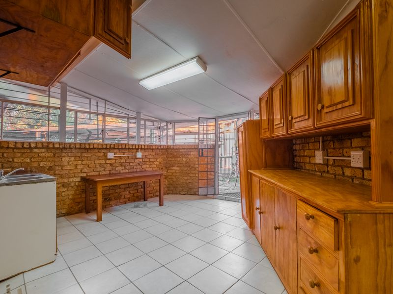 Functional scullery area featuring exposed brick walls, wooden cabinetry, tiled flooring, and direct access to the exterior.