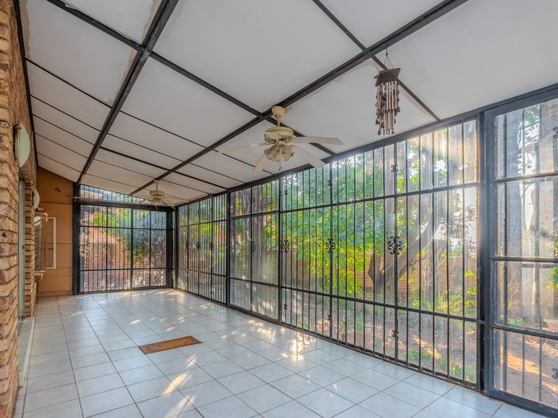 A spacious enclosed patio featuring tiled flooring, ceiling fans, and large windows with security bars, offering a bright view of the garden.