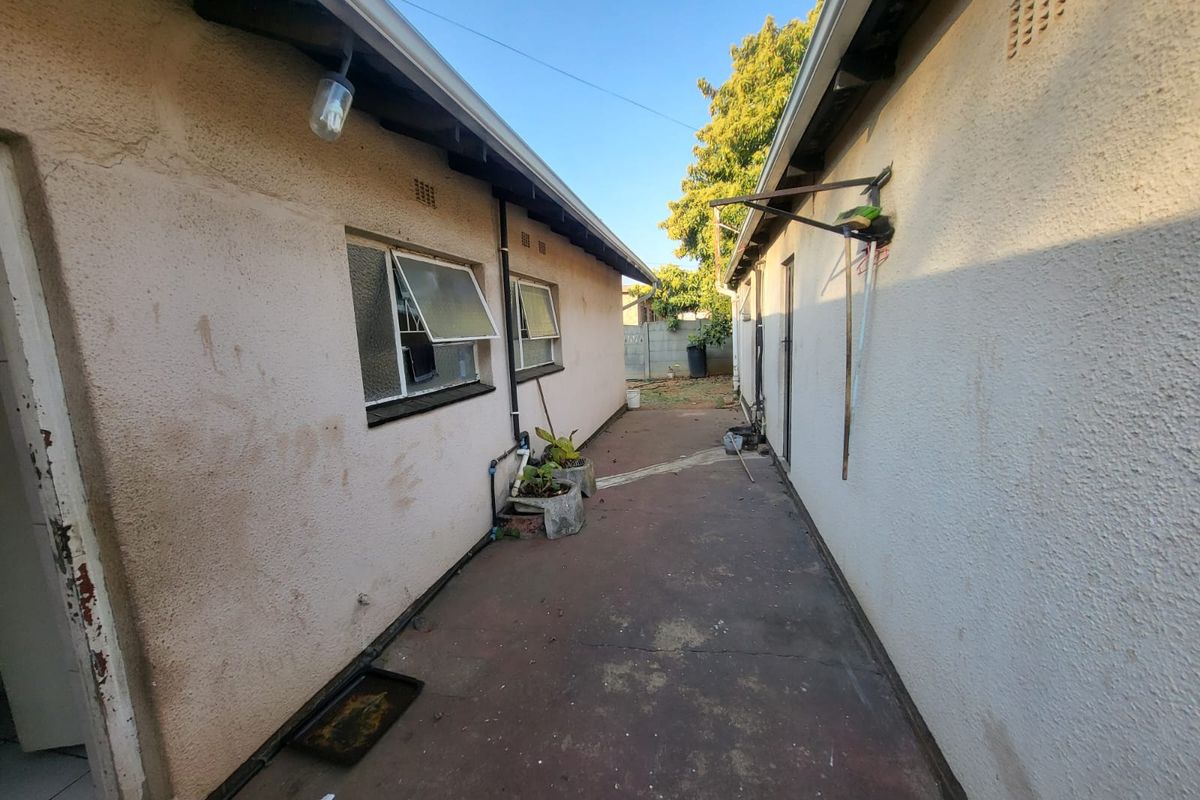 A narrow exterior side passage between two building sections featuring concrete paving and weathered exterior walls.