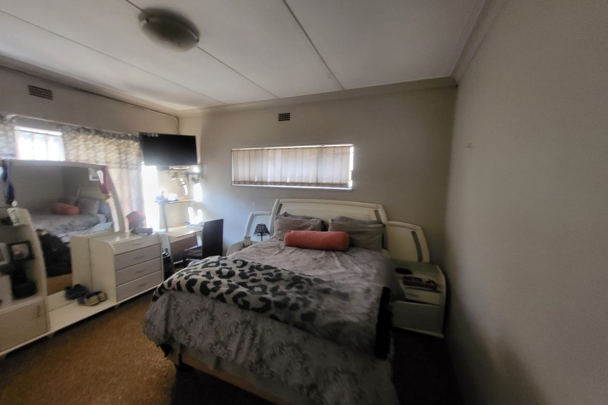 A standard bedroom featuring neutral walls, horizontal window blinds, and a central ceiling light fixture.