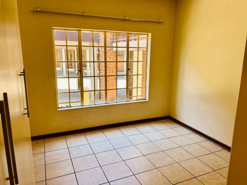An empty bedroom featuring tiled flooring, a steel-framed window, and a built-in cupboard, offering a blank canvas for personalization.