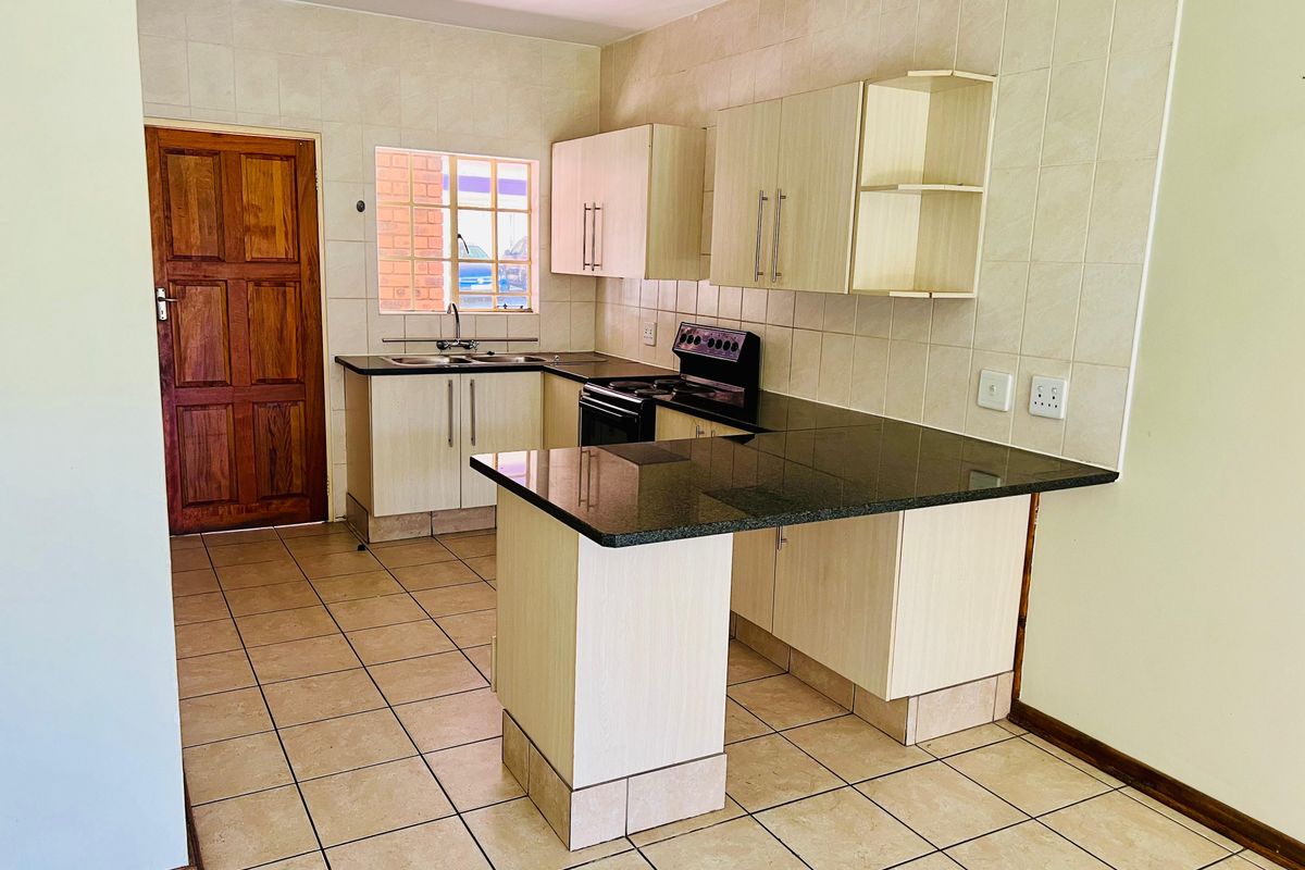 A functional kitchen featuring built-in cabinetry, granite countertops, a double sink, and a freestanding stove, finished with tiled flooring and a tiled backsplash.