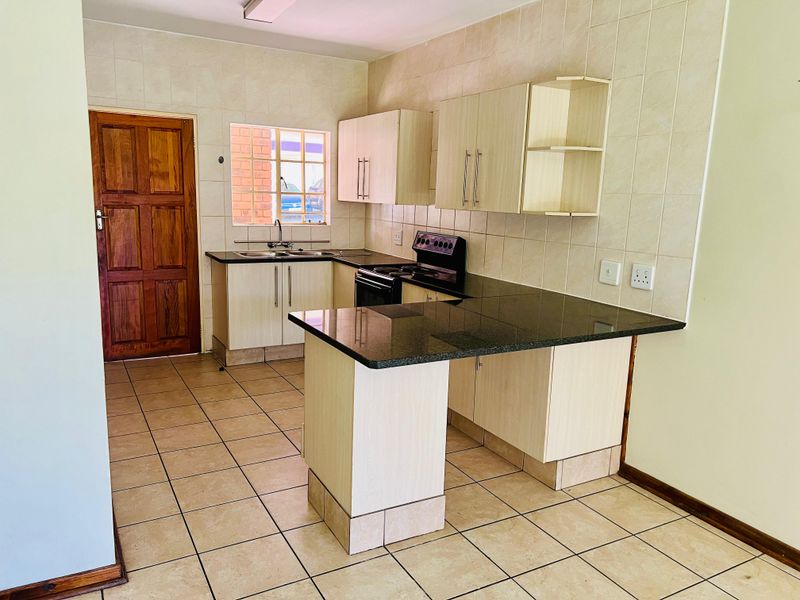 A functional kitchen featuring built-in cabinetry, granite countertops, a double sink, and a freestanding stove, finished with tiled flooring and a tiled backsplash.