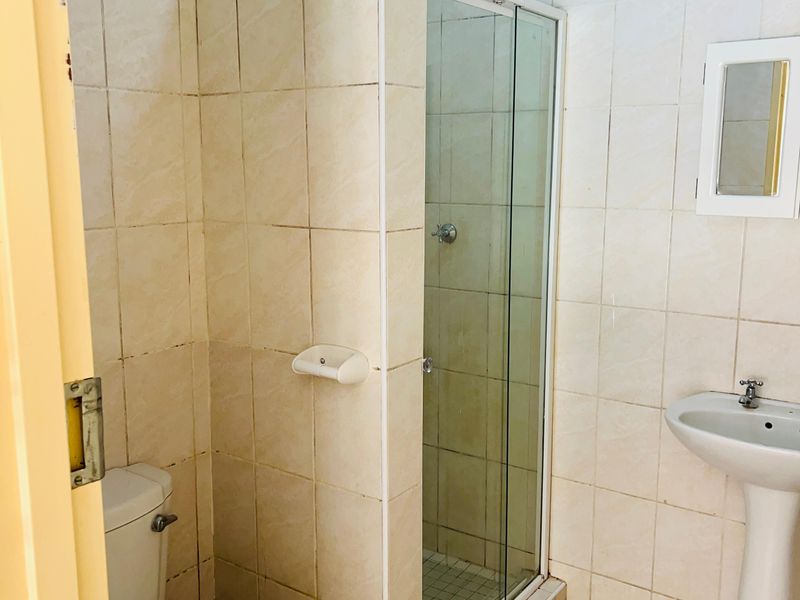 A functional bathroom featuring a pedestal basin, a glass-enclosed shower, and neutral ceramic tiling throughout.