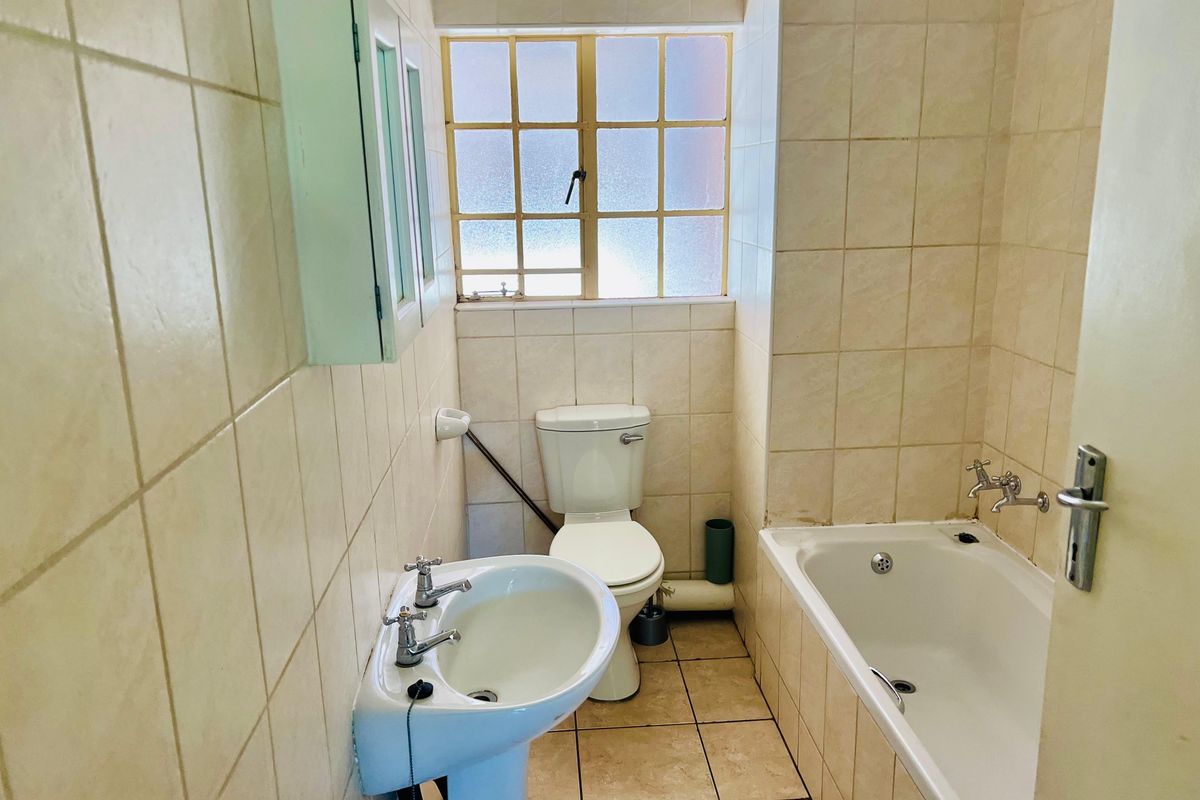 A functional bathroom featuring a pedestal basin, bathtub, and toilet with neutral wall and floor tiling, offering potential for modernization.