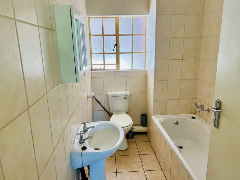 A functional bathroom featuring a pedestal basin, bathtub, and toilet with neutral wall and floor tiling, offering potential for modernization.