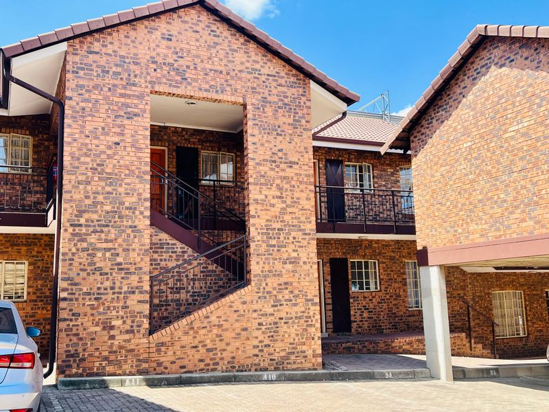Exterior view of a multi-story apartment complex featuring face brick construction, tiled roofing, and an external metal staircase with paved parking access.