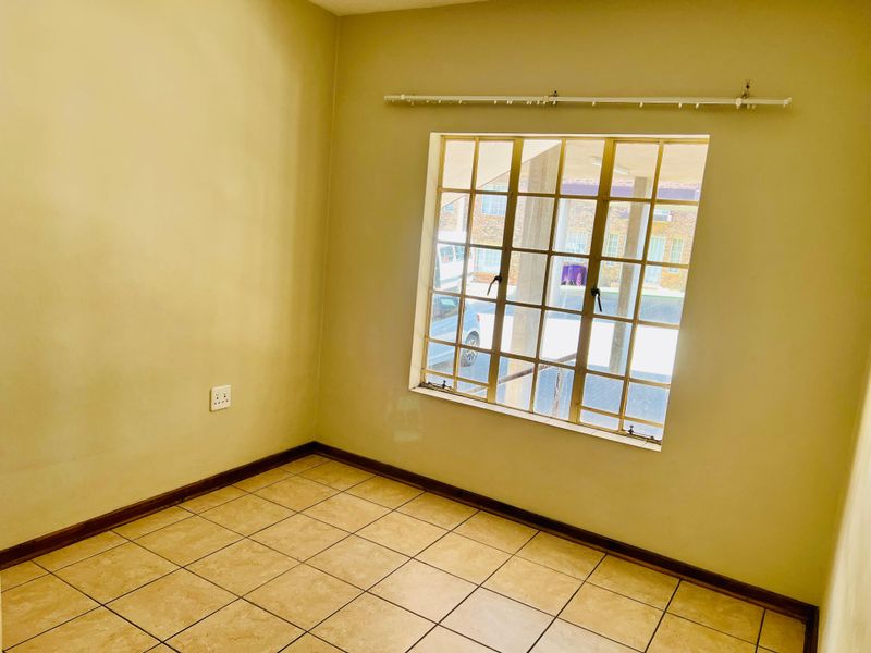 An empty bedroom featuring tiled flooring, a window with security burglar bars, and a curtain rail, offering a blank canvas for personalization.