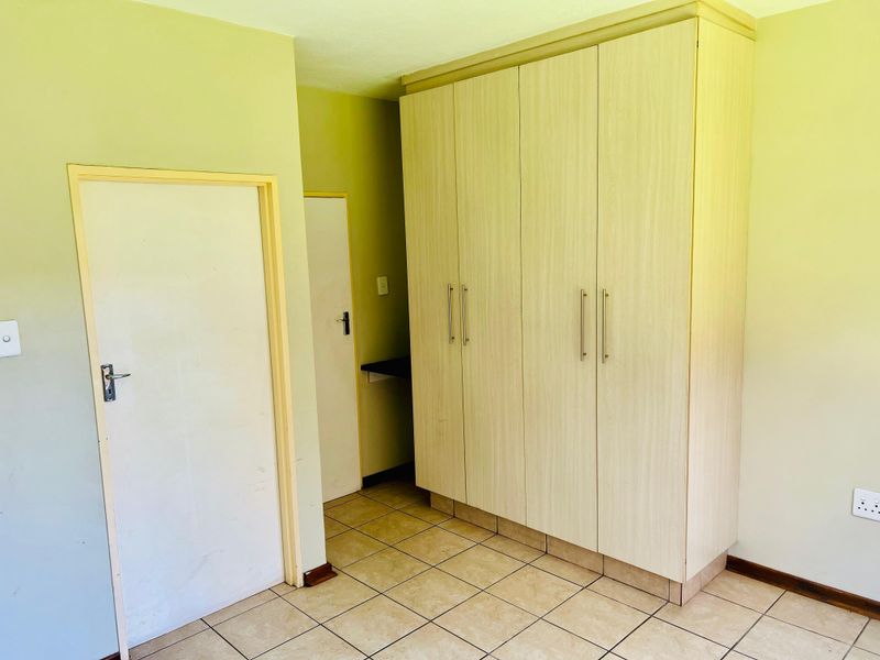 A vacant bedroom featuring light-toned built-in cupboards, tiled flooring, and neutral wall finishes, offering a clean canvas for personalization.