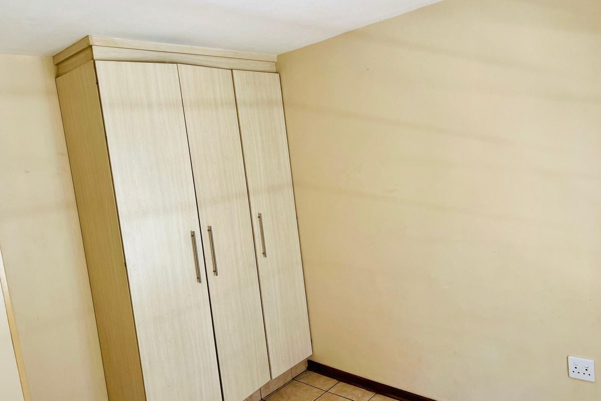 A simple bedroom featuring a light wood-finish built-in wardrobe, tiled flooring, and neutral wall tones, offering a clean and functional space.